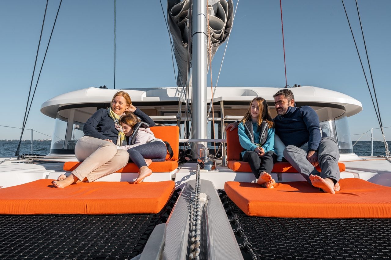 Family sitting on foredeck trampolin of Excess 14 catamaran sailboat