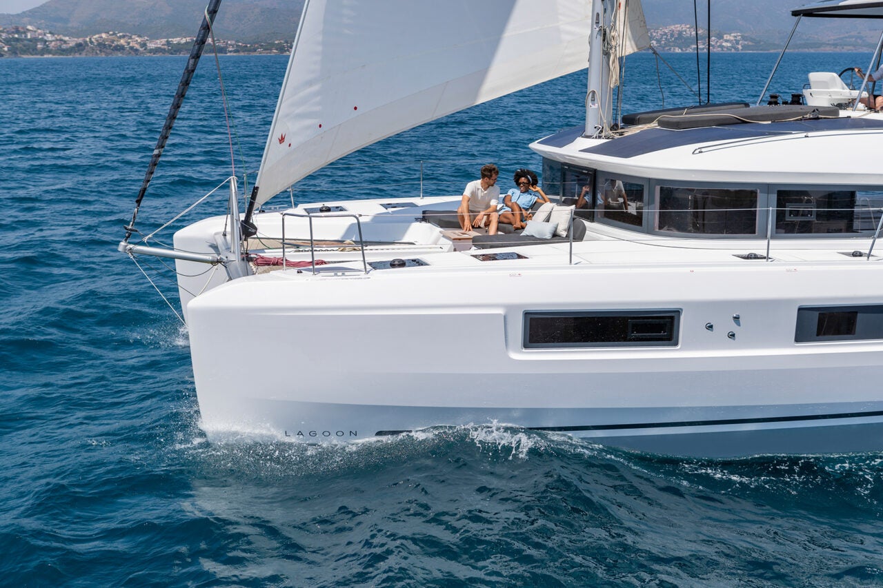 Couple sitting on foredeck lounge of sailing Lagoon 51 catamaran