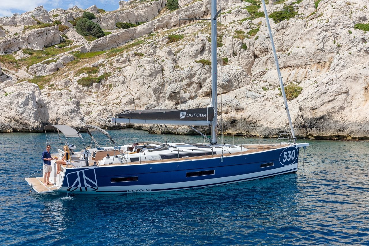 Dufour 530 sailing yacht at anchor with couple on deck relaxing