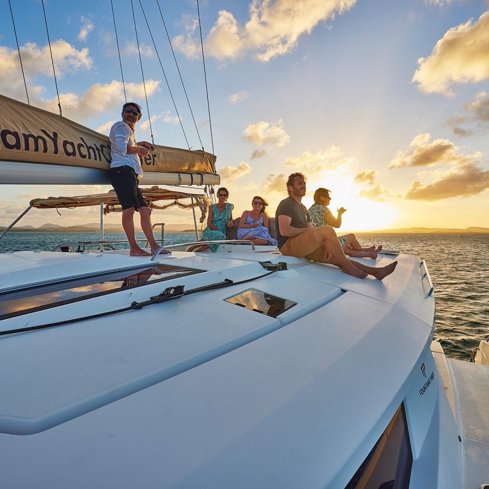 Group of Dream Yacht owners atop a catamaran sailboat at sunset