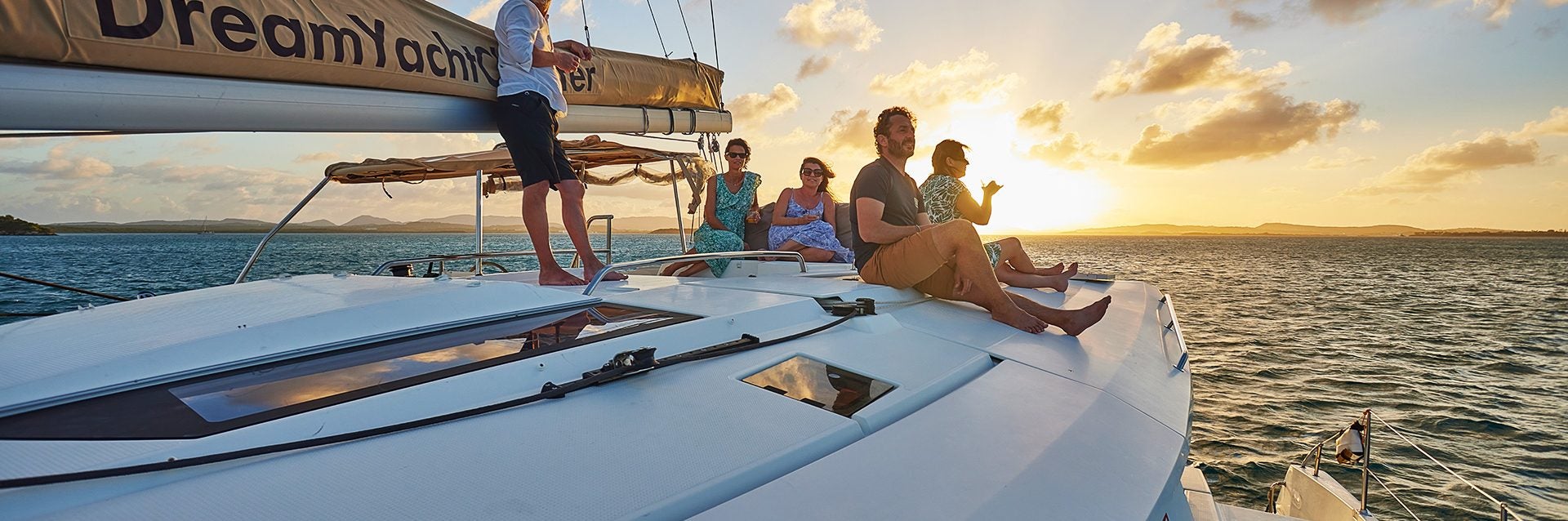 Group of Dream Yacht owners atop a catamaran sailboat at sunset