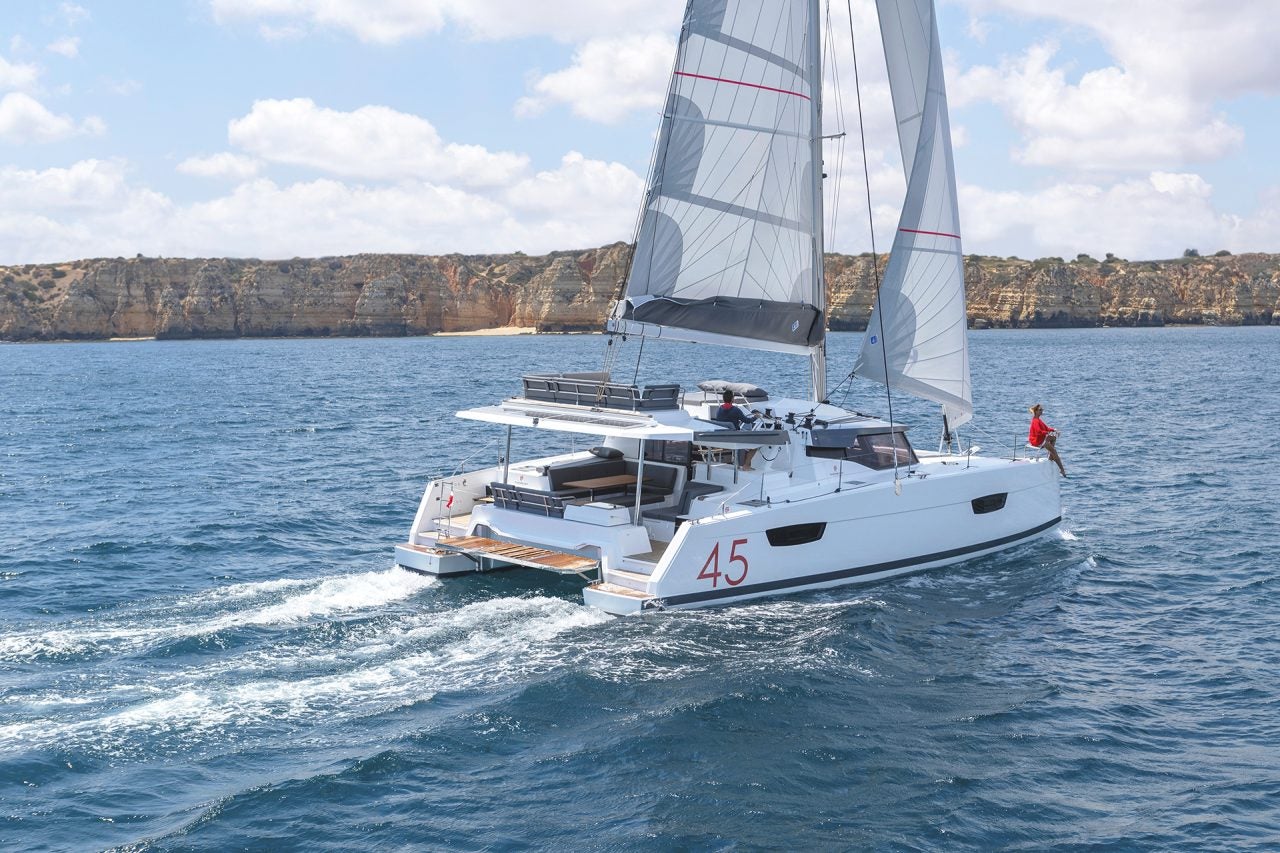 Fountaine Pajot Elba 45 catamaran at sail near rugged cliff coastline